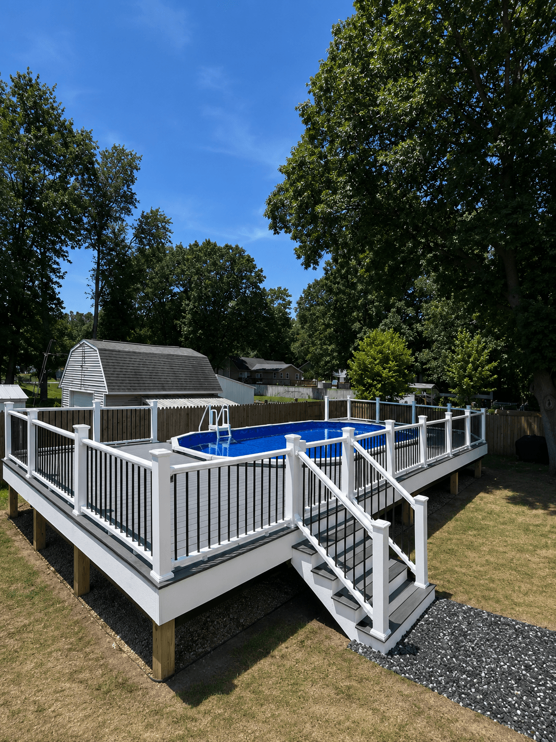 Gray composite deck with white railings and stairs surrounding an oval above-ground swimming pool.