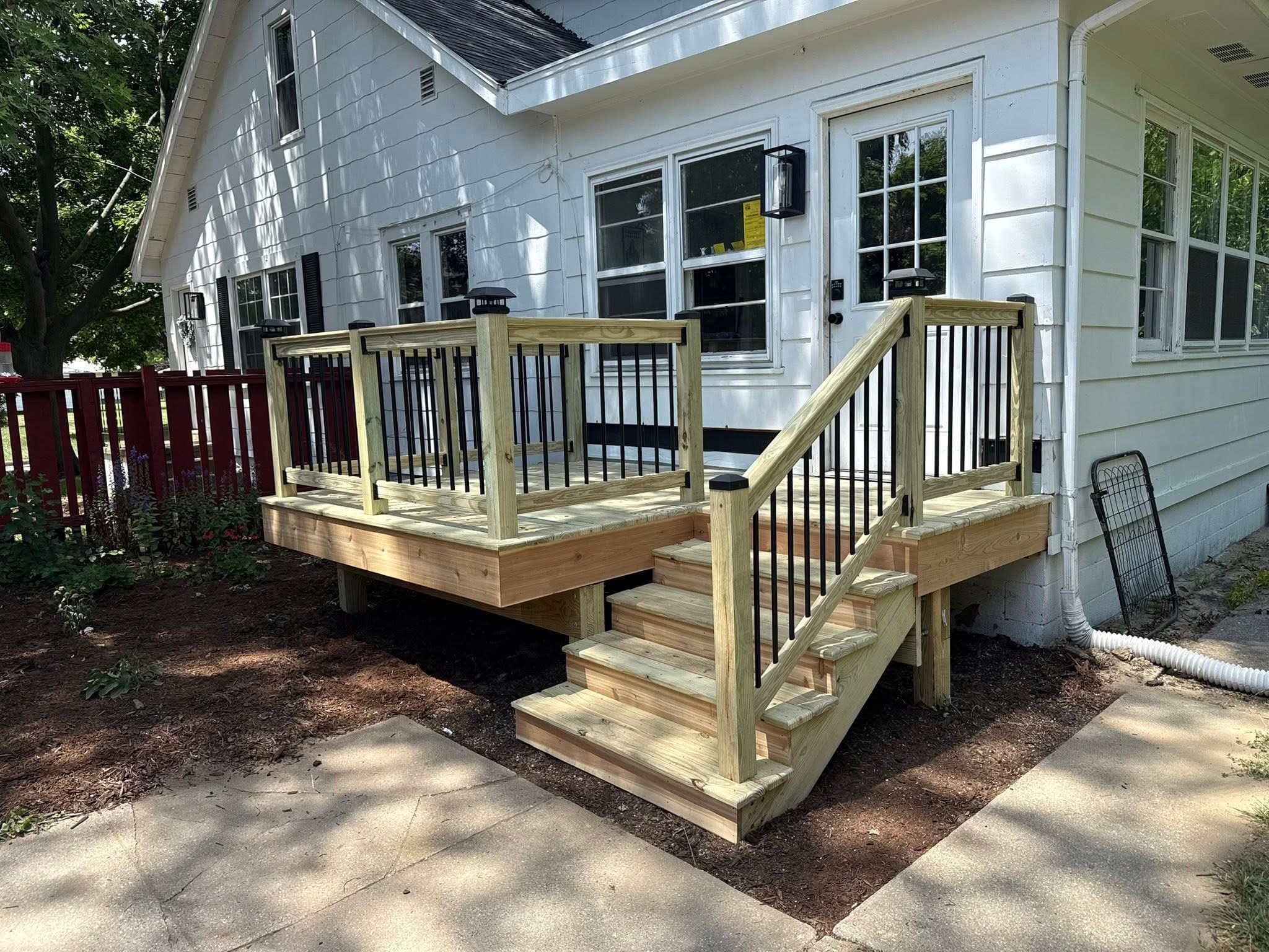 New wooden deck with black metal railings and stairs attached to a white house.