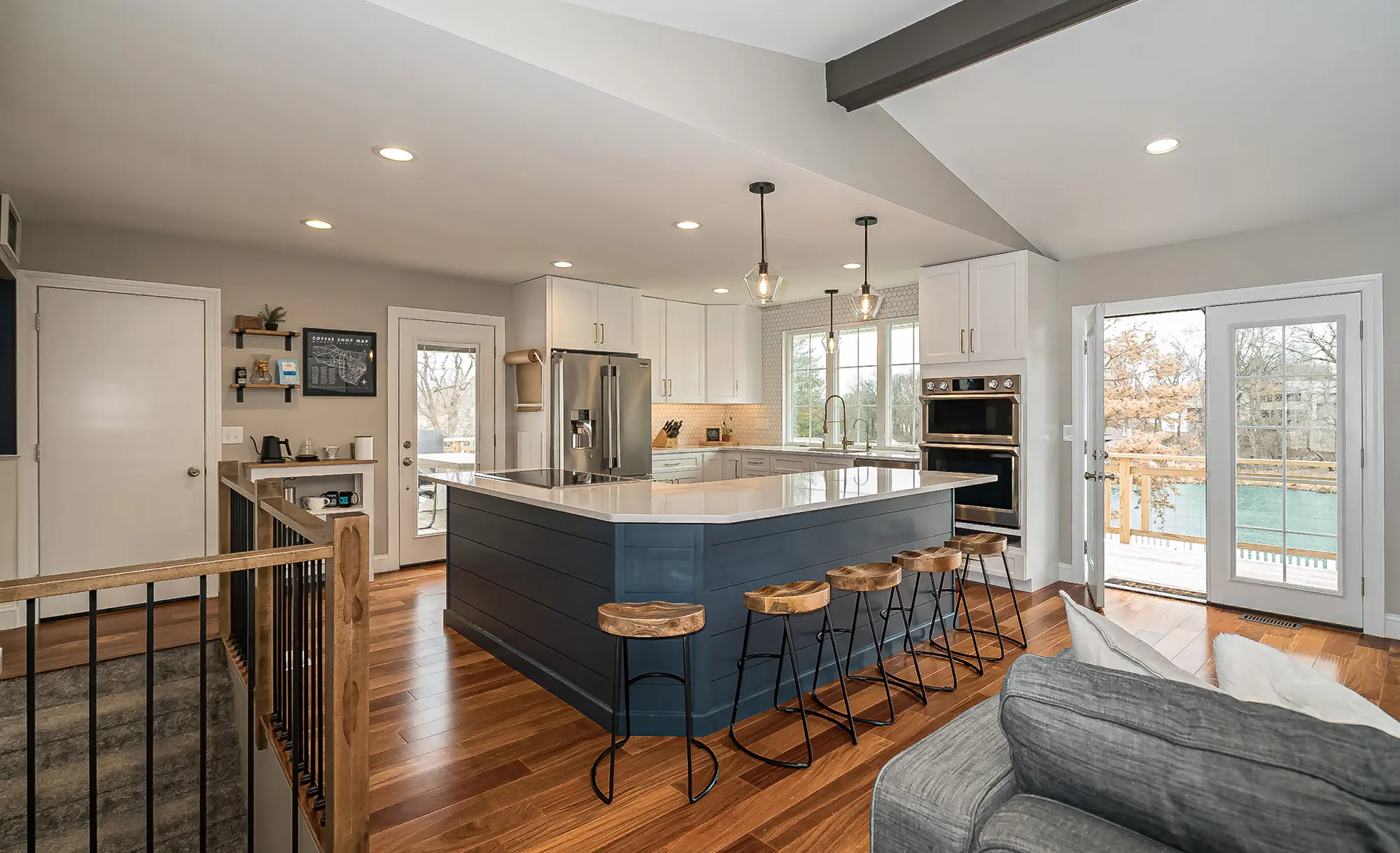 Modern kitchen with a blue island, white cabinetry, hardwood floors, and four wooden bar stools.